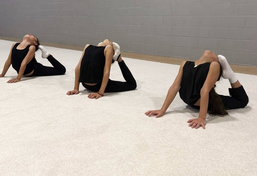 Three young gymnasts practicing bridge backbends together in class