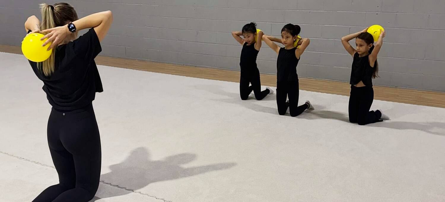 Coach Nastia demonstrating a ball element while her gymnasts mirror her in class
