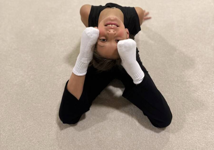 A young gymnast smiling upside down in a kneeling backbend