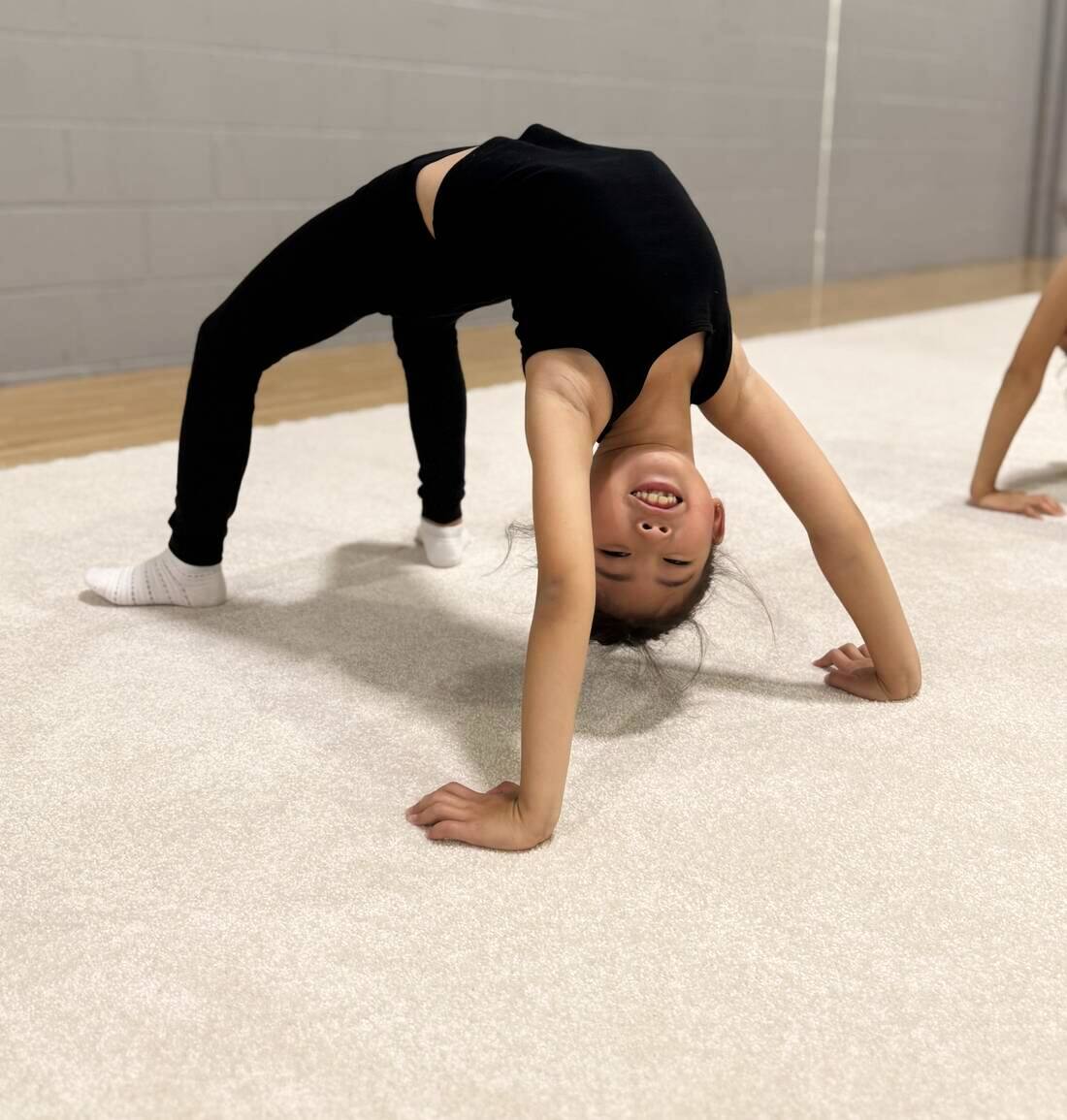 A young gymnast smiling mid-bridge during training at Signature Rhythmic Gymnastics